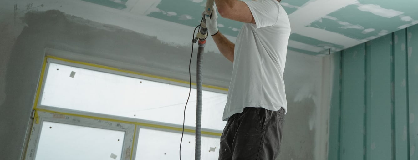 Worker sanding a newly finished drywall ceiling