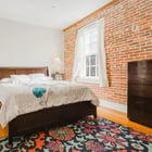 Apartment 303 bedroom with wood bed frame, floral rug and exposed brick