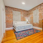 Apartment 303 bedroom with bed, wood dresser and exposed brick