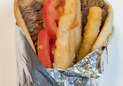 A gyro wrapped in foil with tomato and fries tucked into the pita