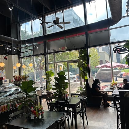 The bright dining room with tall windows, plants and dark wood tables
