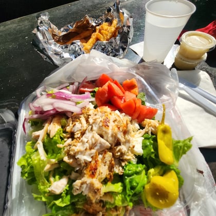 A Greek salad topped with grilled chicken and pepperoncini