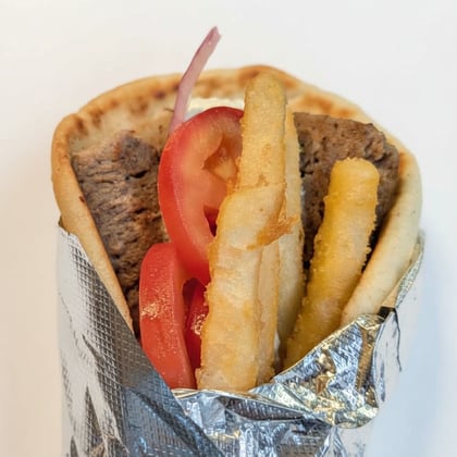 A gyro wrapped in foil with tomato and fries tucked into the pita