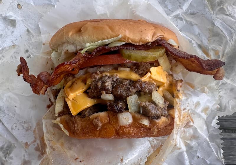 A bacon cheeseburger with pickles and onions on wax paper